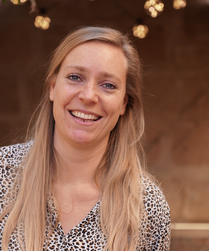 A woman with long blonde hair wearing a patterned shirt and smiling at the camera.